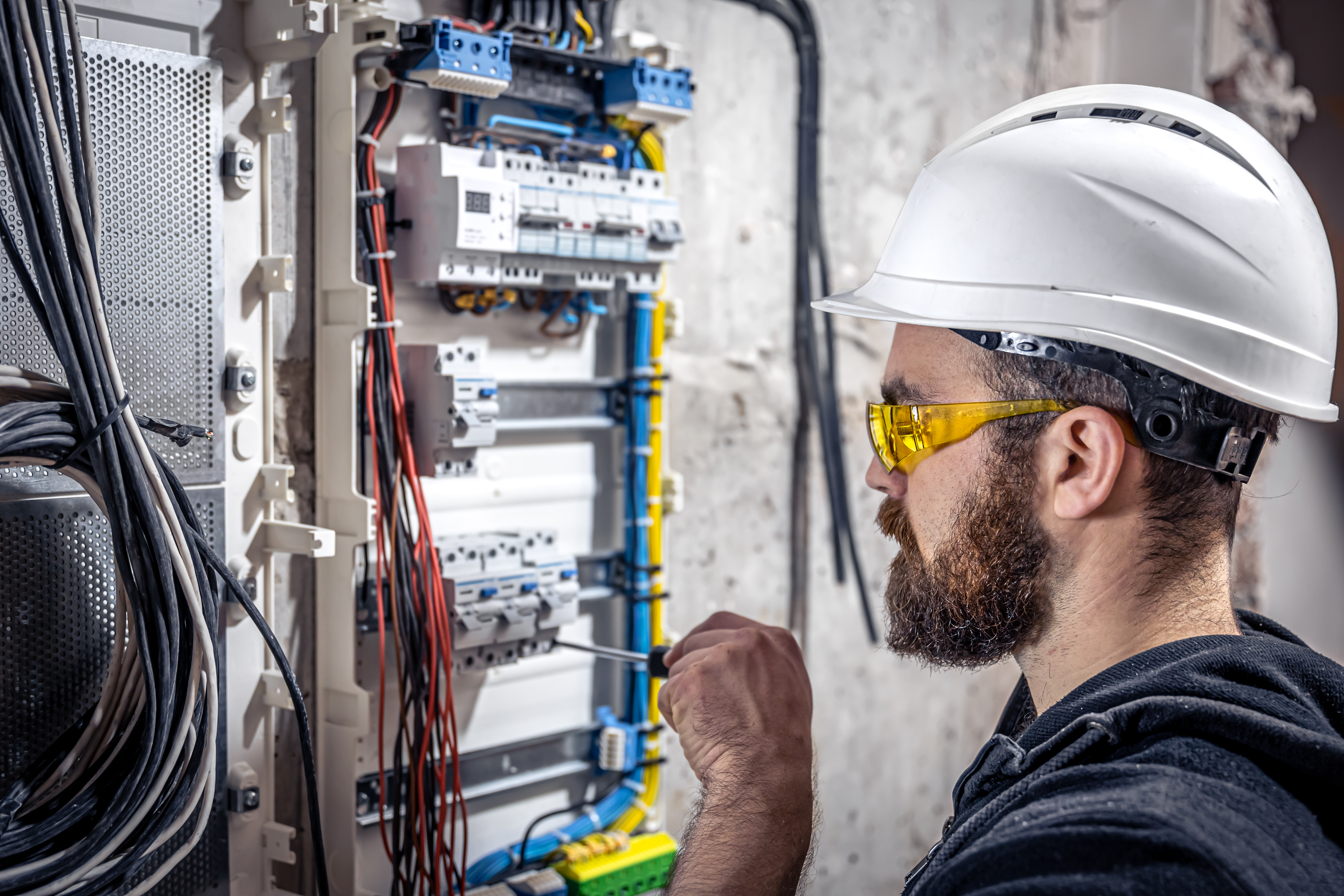A male electrician works in a switchboard with an electrical connecting cable.